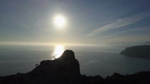 Flight Over of Young Woman Standing on the Top of a Mountain Facing the Sea. Lady on the Summit in