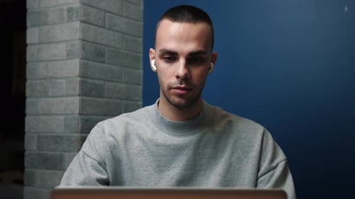 A Focused Young Man Wearing Headphones Is Using His Laptop at Home or Office.