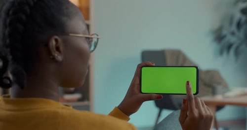 African American Woman Using Smartphone with Green Screen on Couch