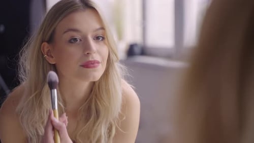 Woman Applying Makeup with Brush Looking in Mirror