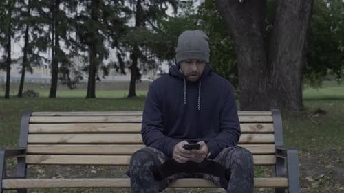 Man Sits on Bench Using Smartphone in Park