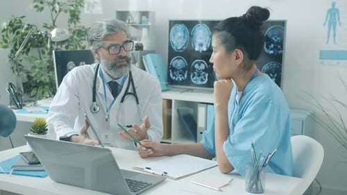 Experienced Doctor Talking to Nurse Showing Tablet Screen Working in Hospital Office