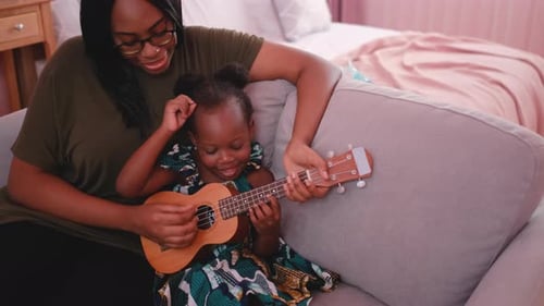 Close up African American mother play ukulele with her child on sofa in bedroom and they look enjoy