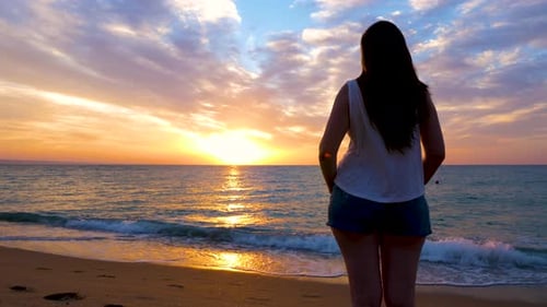 Young Woman Admiring a Gorgeous Vibrant Sunrise on the Beach