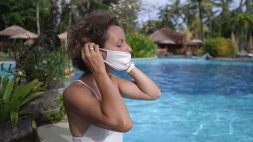Joven mujer blanca usa una máscara facial protectora mientras se relaja en la piscina