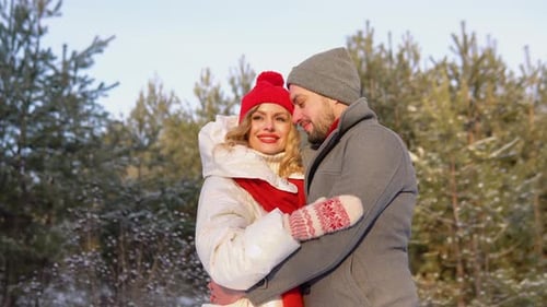 Beautiful Couple in Winter Clothes Hugging in Snowy Forest