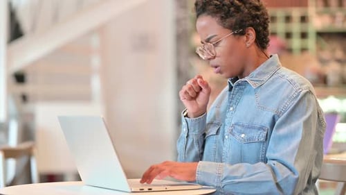 Sick African Woman with Laptop Coughing at Cafe