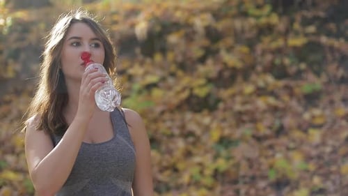 Woman Drinking Water During Outdoor Exercise in Park