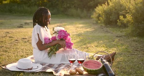 Woman Enjoys Peaceful Picnic with Flowers at Sunset