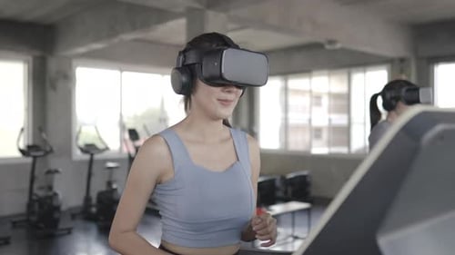 4K Asian athletic woman in sportswear wearing VR glasses jogging on treadmill at fitness gym.