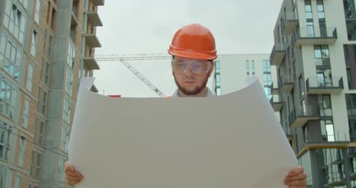 Architect or Builder Man Walking on the Construction Site and Analyzing Scheme Project Plan. Young