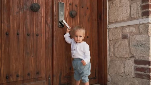 Curious Toddler Stands Near Big Wooden Door Moving Handle