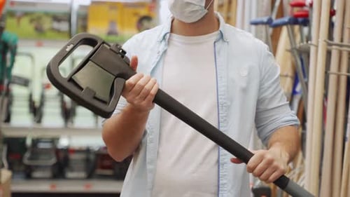 Mann mit medizinischer Maske nimmt in der Bauabteilung eines Einkaufszentrums eine Axt auf