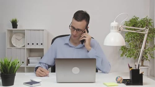 Man Talking on Phone and Taking Notes in Office
