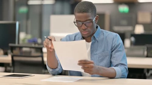 Young African American Man Reading Documents in Office
