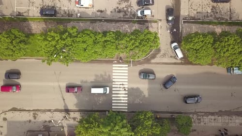 Vista aérea de cima para baixo da rua com carros em movimento e faixa de pedestres com pedestres cruzando.