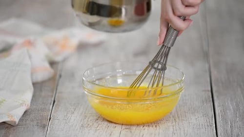 Woman's Hands Close-up Mixing Egg Yolk and Sugar with Whisk in a Large Bowl and Pouring Milk.