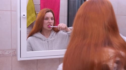 Woman Brushing Teeth in a Bathroom Mirror