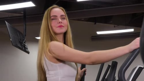 A Young Beautiful Woman Trains on an Elliptical Trainer in a Gym - Closeup From the Side