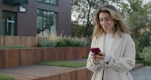 Female Pretty Person Using Smartphone While Walking at City Street. Beautiful Young Woman Typing