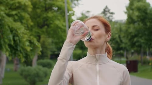 Woman Drinks Water in an Urban Park