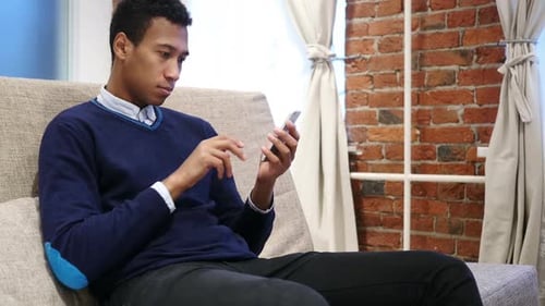 Young Adult Using Smartphone on Sofa Indoors