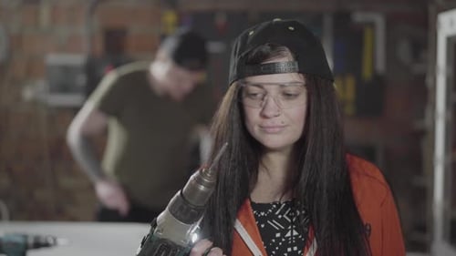 Confident Female Worker Holding a Drill Screwdriver in the Foreground Close Up