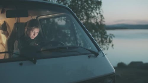Young Woman in Camper Van by Lake at Dusk