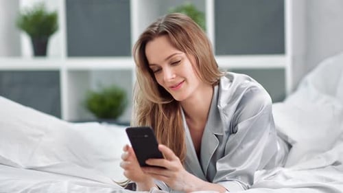 Woman Using Phone Lying on Bed