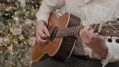 Man Playing Acoustic Guitar by Christmas Tree