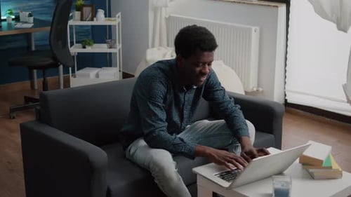 Smiling Man Using Laptop on Couch at Home