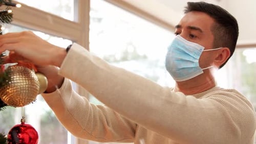 Man Wearing Face Mask Decorates Christmas Tree