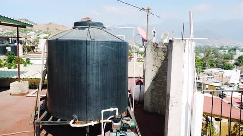 Großer Wassertankcontainer zur Lagerung und Versorgung auf einem typischen Dach in Mexiko. Blauer Himmel und Berge
