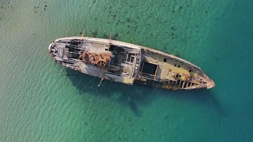 Ein zerstörtes Holzschiff liegt an der Küste, bedeckt mit Rost