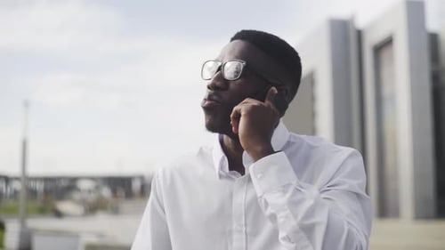 Young African Businessman with Braces and Glasses Talking on Cell Phone in City Park