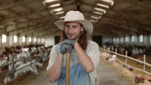 Young Man in Uniform Standing at Goat Farm with Shovel