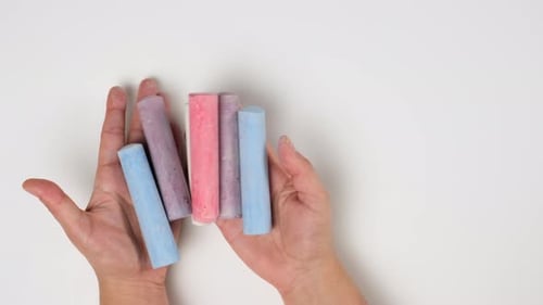 female hands hold multicolored chalk, white background, view from above