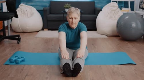 Mature Woman Stretching on Yoga Mat in Living Room