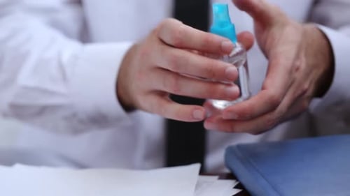 A Worker In A White Shirt And Tie Disinfects His Hands With Aerosol At Work In The Office