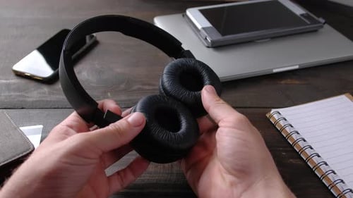 Hands Holding Black Headphones Over a Wooden Desk