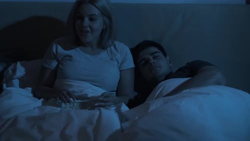 Woman Eating Popcorn While Man Sleeps in Bed