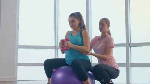 Schwangere Frau macht Yoga-Ball-Übungen mit einer Langhantel in jeder Hand
