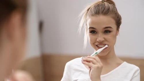 Blonde Woman Brushing Teeth in Bathroom Mirror