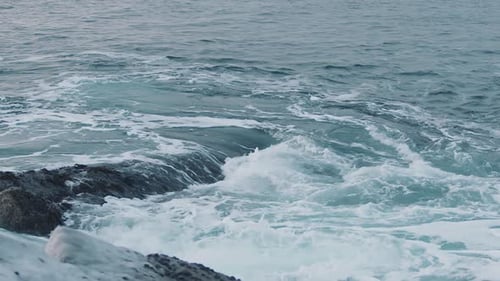 Stormy Sea Waves Roll Over Boulders on the Shore and Twist Into Whirlpools