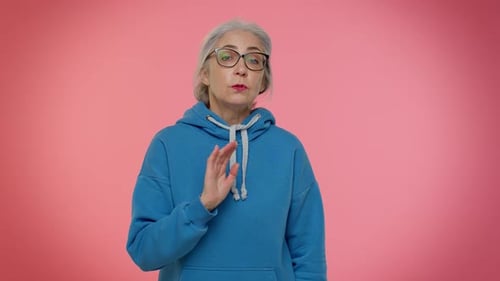 Ältere alte Frau zeigt mit verspieltem, fröhlichem Ausdruck auf die Kamera und zeigt die Richtung