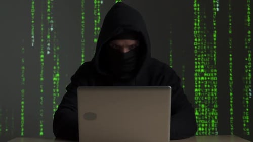 Mysterious Hooded Figure Hacking Computer with Matrix Background