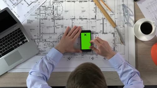 Male Architect Scrolling on Smartphone With Green Screen at Workplace, Top View
