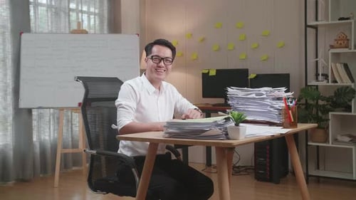 Asian Man Smiling To Camera While Working With Documents At The Office