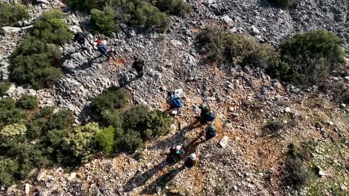 People Explore Rocky Terrain on a Sunny Hillside