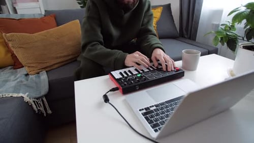 Man Playing a Keyboard Connected to Laptop at Home